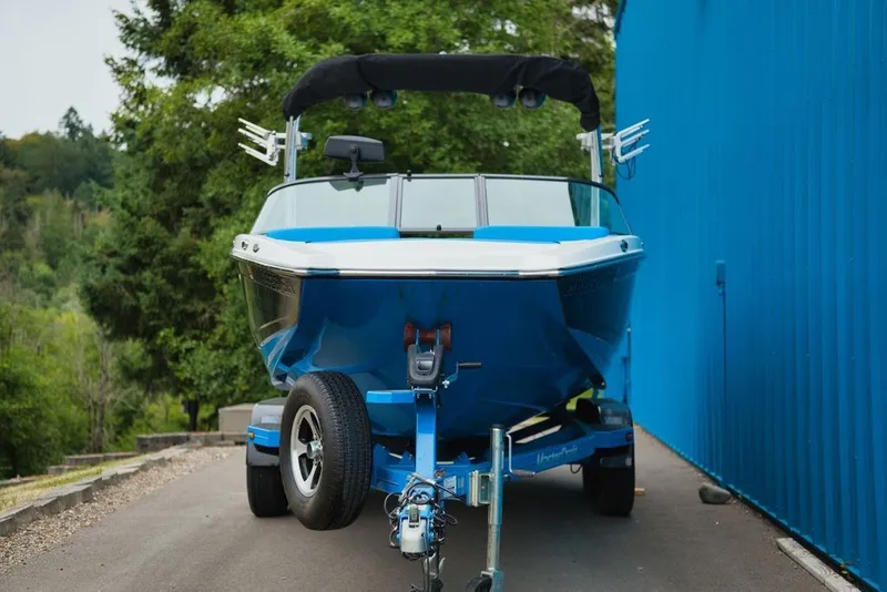 Slide: The Image of A blue 2016 MasterCraft NXT20 on a trailer beside a blue building. - 2