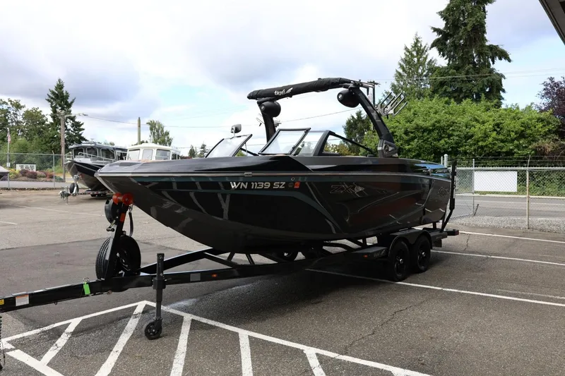 Slide: The Image of 2021 Tigé 23ZX boat on trailer in parking lot, surrounded by trees and other boats. - 7