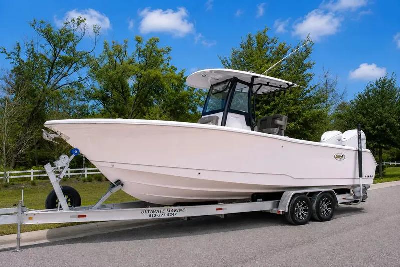 The Image of A 2027 Sea Hunt Gamefish 25 boat on a trailer, surrounded by trees and blue sky. - 1