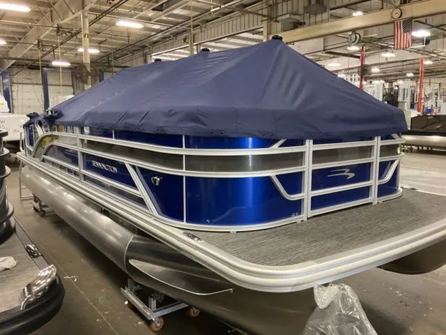 Slide: The Image of A Bennington pontoon boat with a blue cover is in a warehouse. - 14