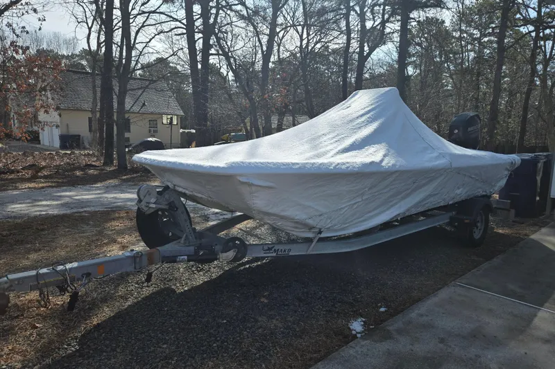 Slide: The Image of 2014 Mako Pro Skiff 17 CC boat covered on trailer in wooded area. - 4