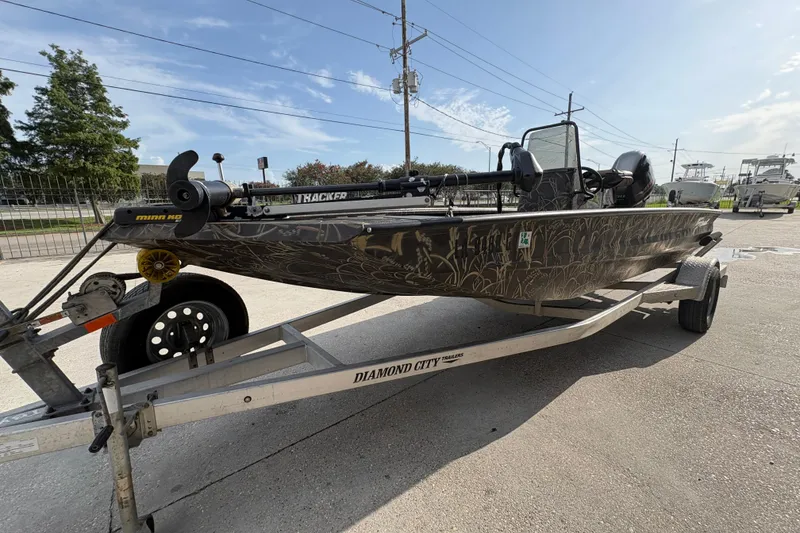 Slide: The Image of 2018 Excel 1854 Shallow Water F4 Console boat on trailer, camo design, outdoor setting. - 7