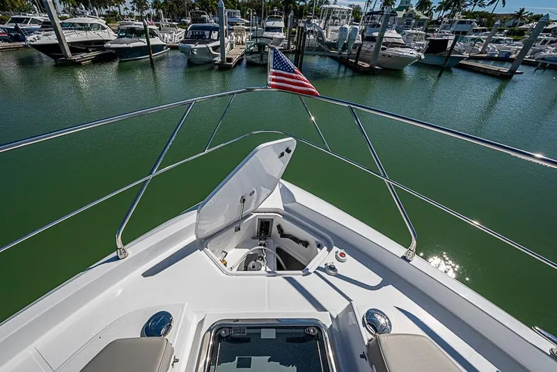 Slide: The Image of Bow view of 2025 Cruisers Yachts 50 Cantius in marina, featuring open hatch and American flag. - 55