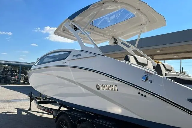 Slide: The Image of 2021 Yamaha Boats 275SD on trailer, sleek design, white exterior, sunny day background. - 2