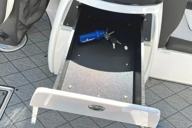 Slide: The Image of Open storage compartment in 2021 Yamaha Boats 275SD with keys and blue item inside. - 26