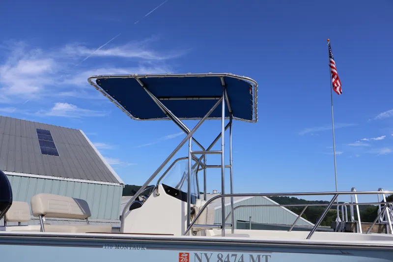 Slide: The Image of 2023 Boston Whaler 170 Montauk boat with canopy, American flag, and clear blue sky. - 17