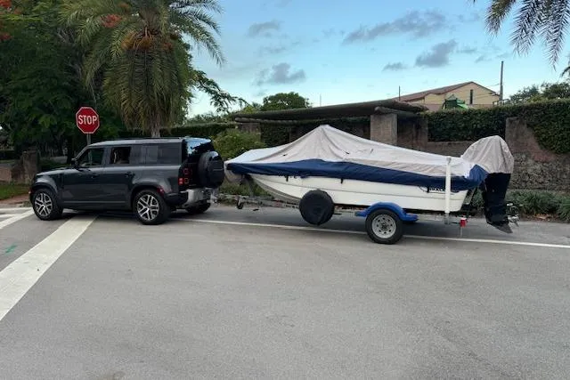 Slide: The Image of SUV towing a covered 2016 Boston Whaler 150 Montauk boat on a trailer at an intersection. - 2