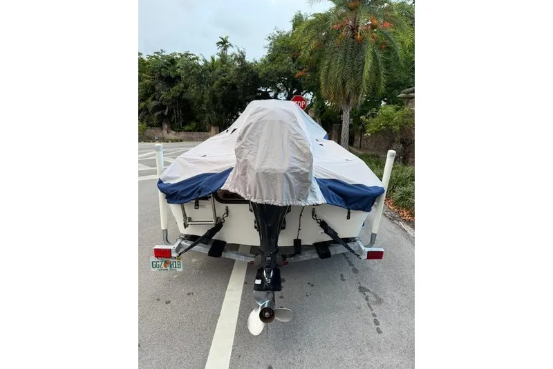 Slide: The Image of Covered 2016 Boston Whaler 150 Montauk boat on trailer, parked near tropical trees. - 5