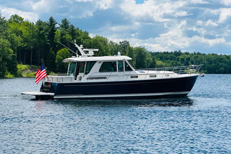 The Image of 2025 Sabre 48 Salon Express yacht on a serene lake with lush green forest backdrop. - 0