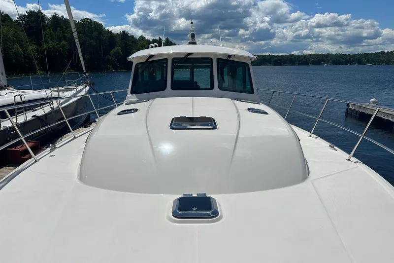 Slide: The Image of 2025 Sabre 48 Salon Express yacht docked on a serene lake under a partly cloudy sky. - 87