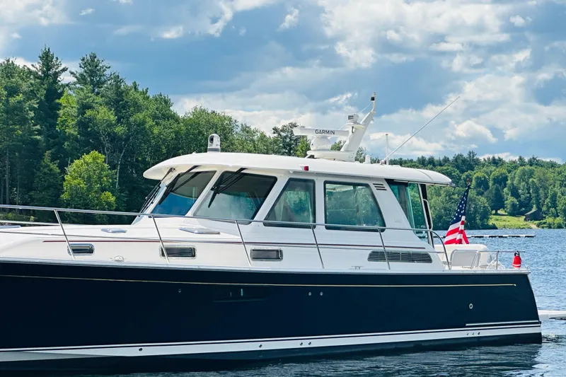 Slide: The Image of 2025 Sabre 48 Salon Express yacht cruising on a serene lake with lush green trees. - 93