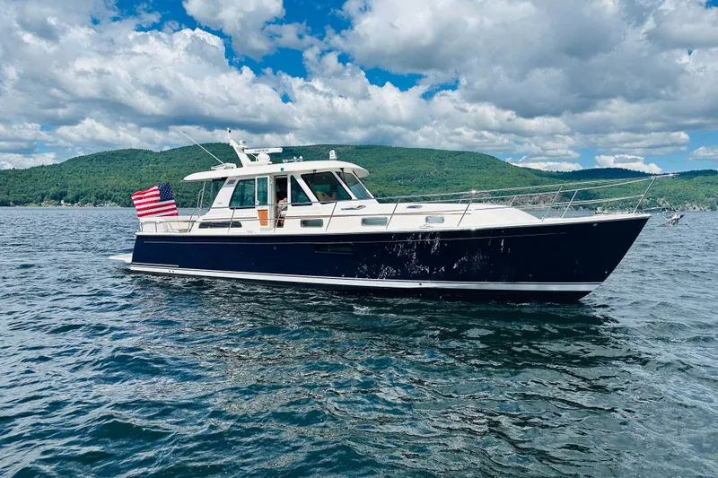 Slide: The Image of 2025 Sabre 48 Salon Express yacht cruising on a scenic lake under a cloudy sky. - 96