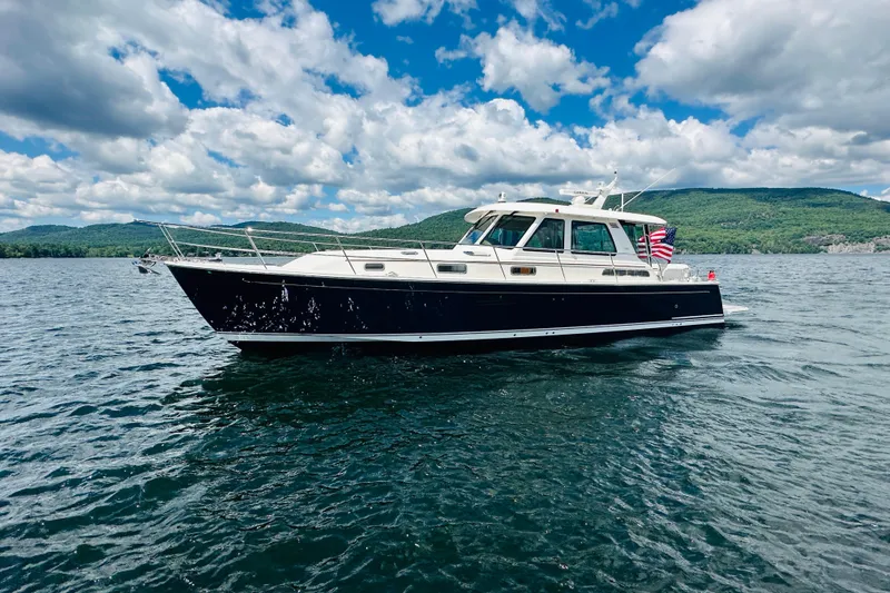 Slide: The Image of 2025 Sabre 48 Salon Express yacht cruising on a scenic lake under a partly cloudy sky. - 98