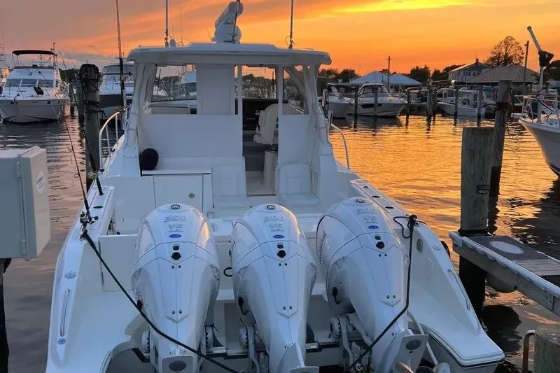 Slide: The Image of 2023 Pursuit OS 355 Offshore boat docked at sunset with triple outboard engines. - 2