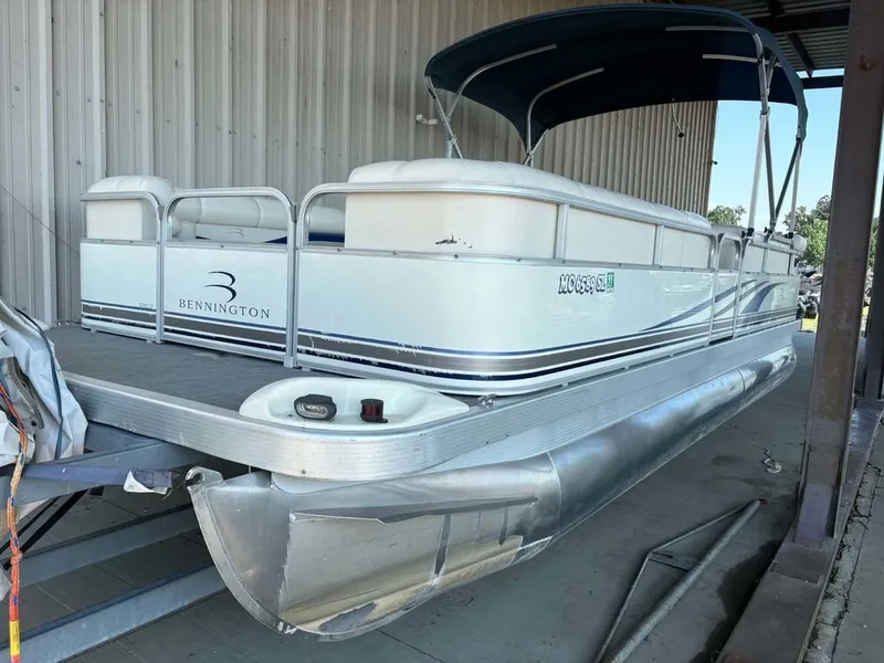 The Image of A 2002 Bennington 2250 LX pontoon boat is parked in a covered area. It features a blue canopy. - 1