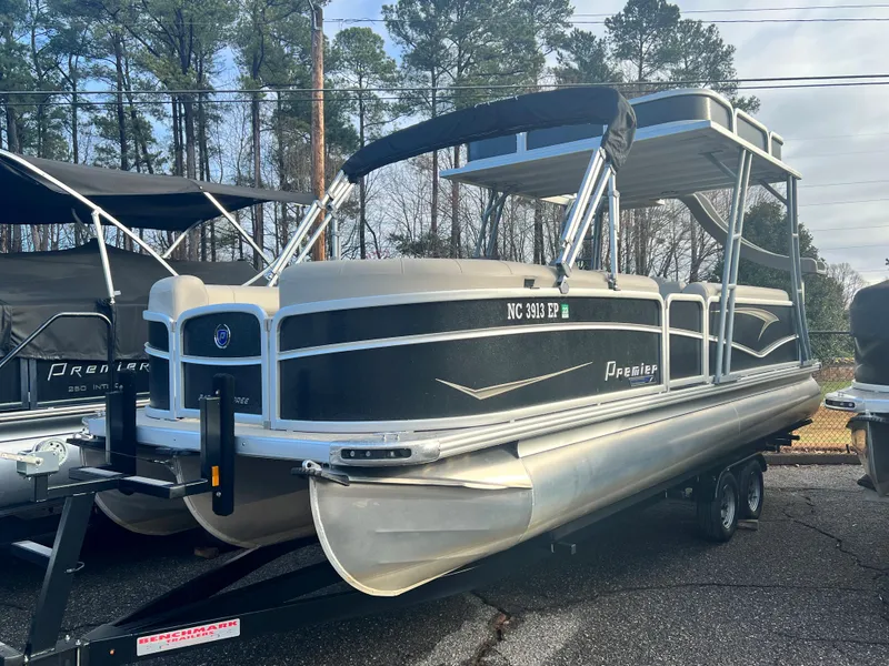 The Image of A 2020 Premier 240 SunSpree Water Slide pontoon boat on a trailer, surrounded by trees. - 1