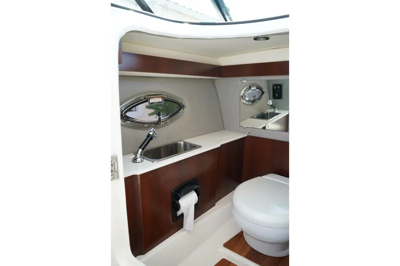 Slide: The Image of 2025 Chaparral 270 OSX boat interior bathroom with sink, toilet, and wooden accents. - 4