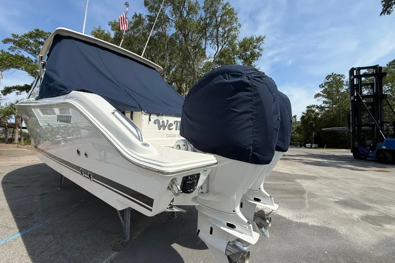 Slide: The Image of 2024 Pursuit DC 306 Dual Console boat with covered engines, parked outdoors. - 3