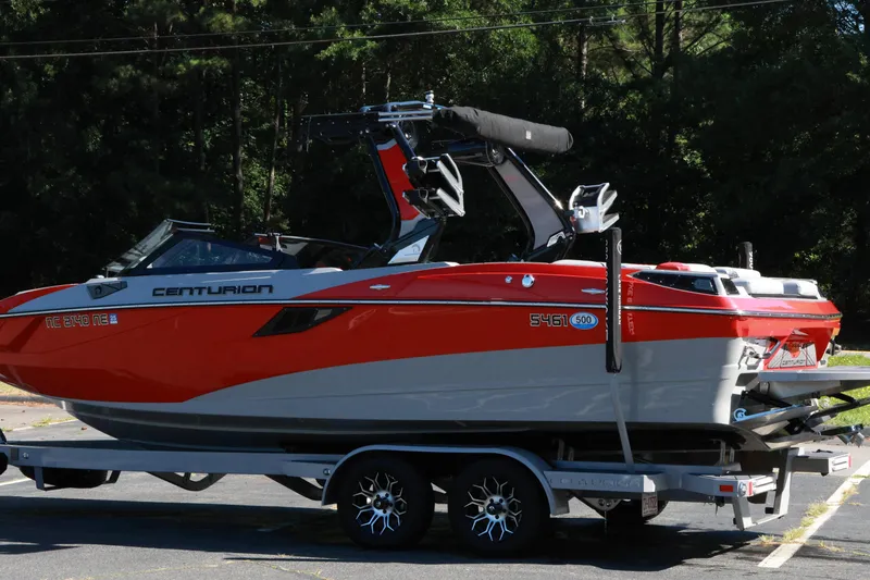 Slide: The Image of 2024 Centurion Fi23 boat in vibrant red and gray on a trailer, parked outdoors. - 20
