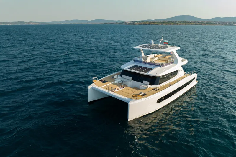 Slide: The Image of 2025 Custom Omaya 50 Power Catamaran cruising on open sea with scenic coastline backdrop. - 7