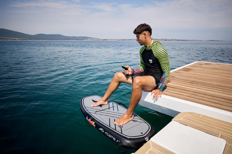 Slide: The Image of Man sitting on Omaya 50 Power Catamaran, holding phone, with water and mountains in background. - 33
