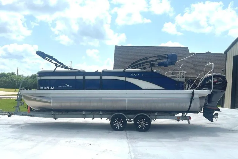 The Image of 2023 Bennington 23 SX pontoon boat on trailer, parked outdoors under a cloudy sky. - 1