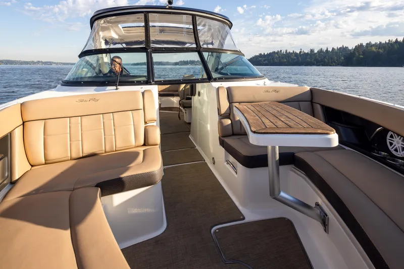 Slide: The Image of 2016 Sea Ray SLX 350 boat interior with tan seating and wooden table on a sunny day. - 16