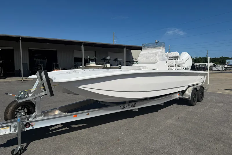 Slide: The Image of 2026 Skuta 24 Cat boat on trailer, parked outside a warehouse under clear blue sky. - 3