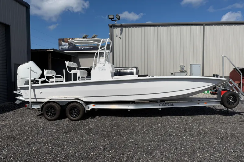 The Image of 2026 Skuta 24 Cat boat on trailer, parked outside industrial building under blue sky. - 0