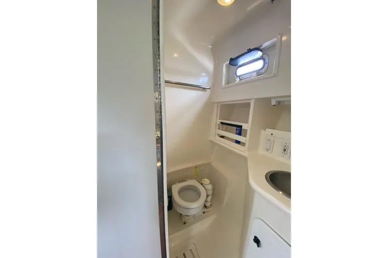 Slide: The Image of 1996 Pursuit 3000 Offshore boat bathroom with toilet, sink, and storage shelves. - 13