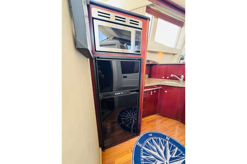 Slide: The Image of 2006 Sea Ray 44 Sedan Bridge yacht kitchen with microwave, fridge, and wooden cabinetry. - 18
