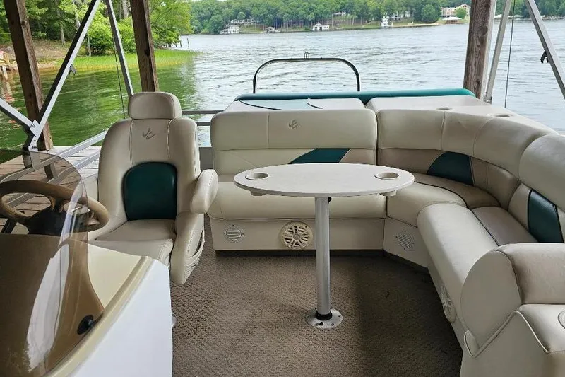 Slide: The Image of 2006 JC NepToon 23 TT pontoon boat interior with plush seating and table, docked by a lake. - 5