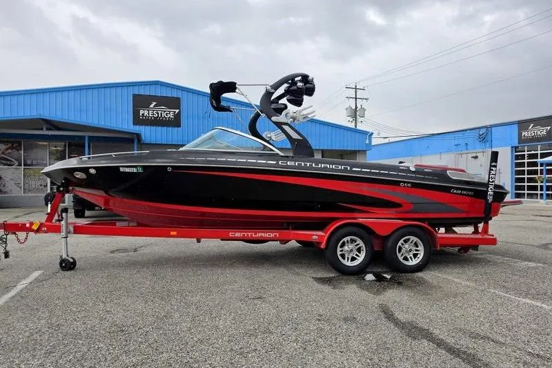 The Image of 2012 Centurion Enzo SV233 boat on red trailer, parked outside blue building. - 1