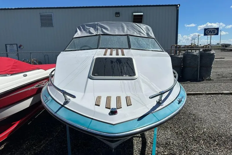 The Image of 1992 Reinell 192 RM boat with covered windshield, parked outdoors on gravel. - 1