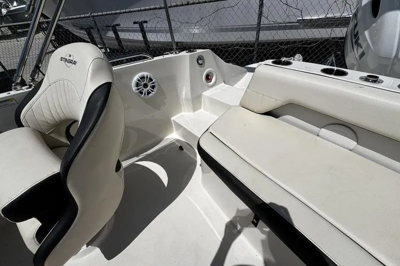 Slide: The Image of 2022 Stingray 212 SC boat interior with seating and speaker, parked near a fence. - 24