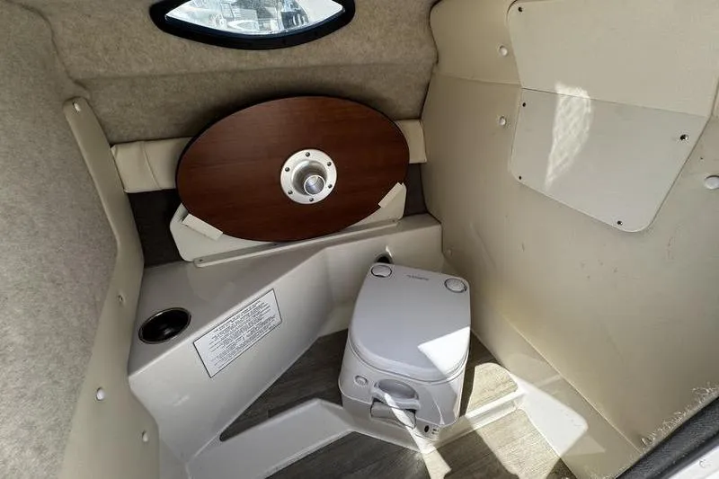 Slide: The Image of 2022 Stingray 212 SC boat interior with portable toilet and wooden table. - 18
