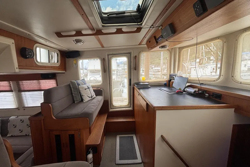 Slide: The Image of Interior of a 2004 Nordic Tug 37, featuring cozy seating and a navigation desk. - 11