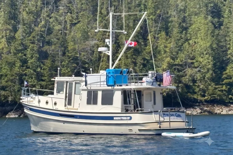 The Image of 2004 Nordic Tug 37 boat on water, surrounded by lush forest, displaying Canadian and American flags. - 0