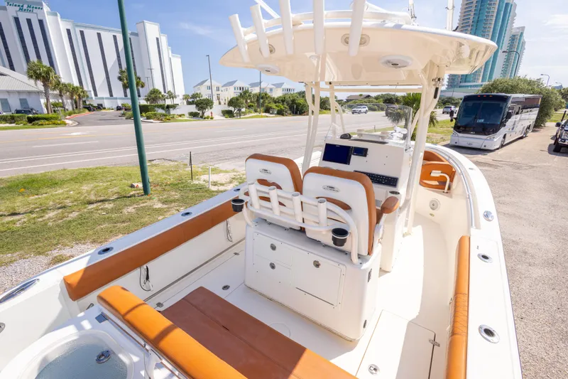 Slide: The Image of 2017 Cobia 261 Center Console boat with tan seating, parked near a road and buildings. - 20