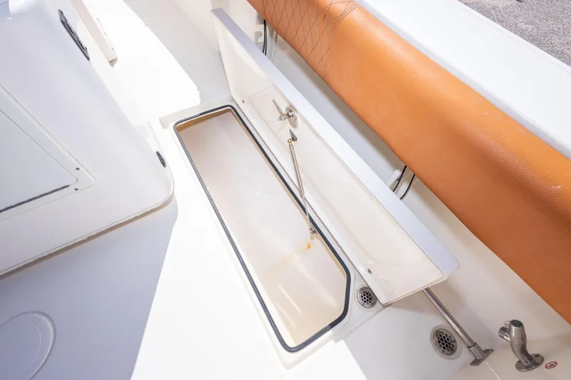 Slide: The Image of 2017 Cobia 261 Center Console boat storage compartment with tan cushion and white interior. - 46