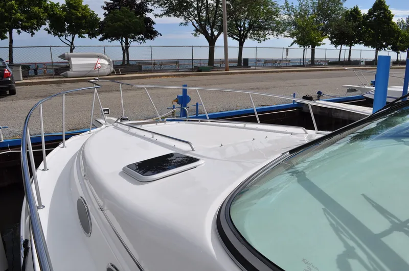 Slide: The Image of A 1999 Doral 350sc docked. The foredeck area is visible, surrounded by trees and a fence. - 3
