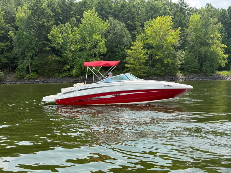 Slide: The Image of A red 2009 Sea Ray 230 Sundeck boat cruising on a calm lake with a wooded backdrop. - 0