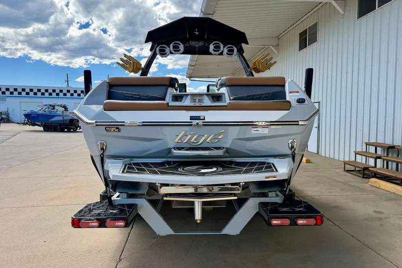 Slide: The Image of 2025 Tigé Ultré 25ZX boat rear view at a marina under a cloudy sky. - 5