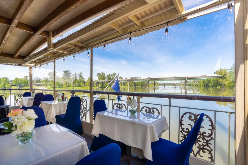 Slide: The Image of An elegant dining area on a boat overlooking a river and a bridge. - 50