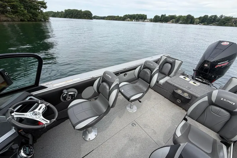 Slide: The Image of 2023 Lund 1975 Tyee boat interior with seating and steering wheel on a calm lake. - 8