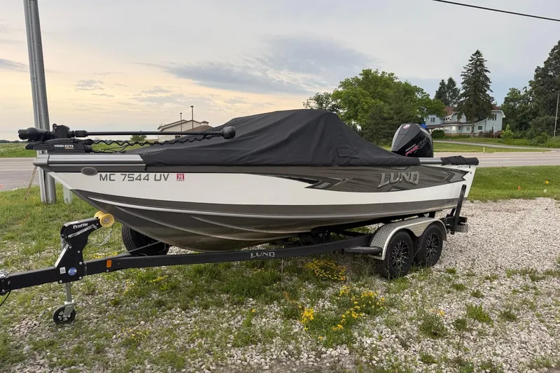 The Image of 2023 Lund 1975 Tyee boat on trailer, covered, parked on gravel near road. - 0