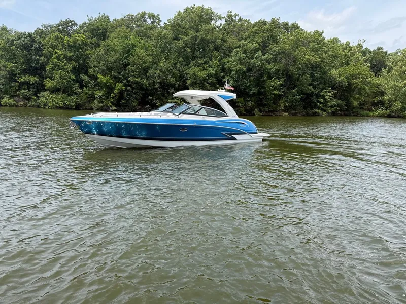 The Image of A blue and white bowrider glides on a calm river, surrounded by lush greenery. - 0