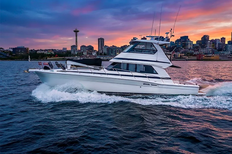 Slide: The Image of 1999 Riviera 48 Convertible yacht cruising at sunset with city skyline backdrop. - 74