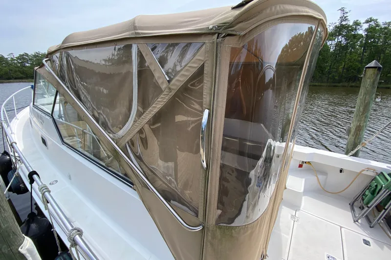 Slide: The Image of 2002 Mainship Pilot 34 boat with tan canvas enclosure docked by a serene river. - 47
