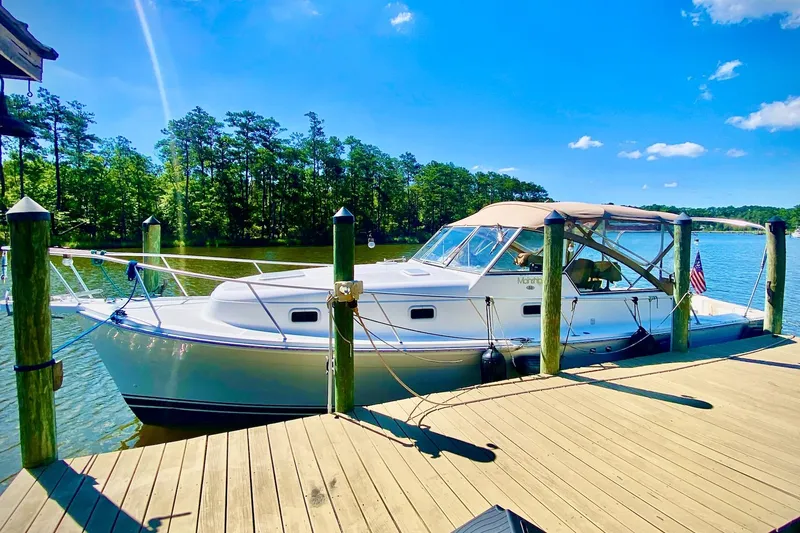 The Image of 2002 Mainship Pilot 34 docked by a scenic lake under a clear blue sky. - 0